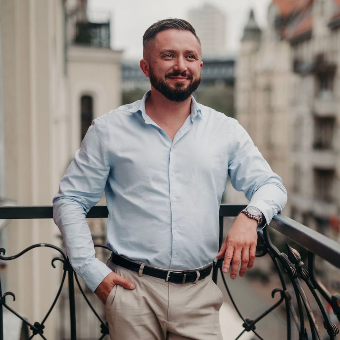 Robert Rał w jasnej koszuli na balkonie kamienicy, uśmiechnięty